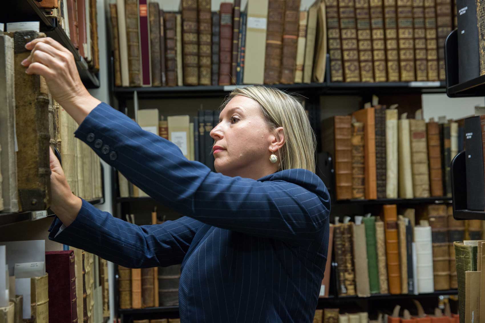 UCSF Archivist Polina Ilieva pulls out a leather bound book from a bookstack at Kalmanovitz Library.
