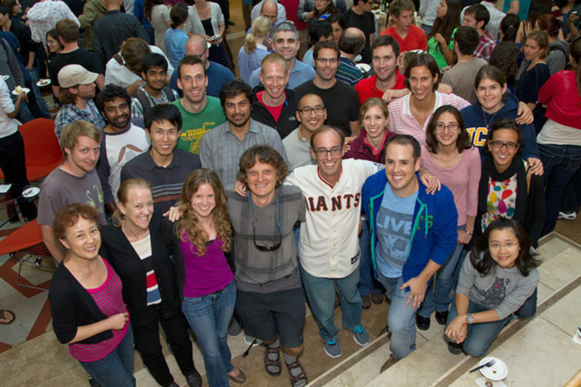 Ronald Vale, PhD, wearing a Giants jersey is smiling for the camera with his colleagues in the lobby of Genentech Hall
