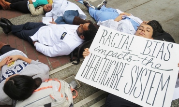 Student laying down holding a sign 'Racial Bias impacts the Healthcare System'.