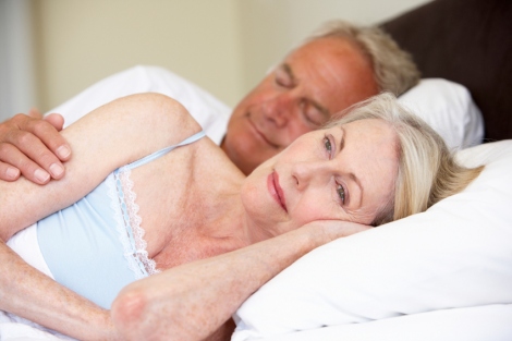 stock image of couple in bed, with the man asleep and the woman awake