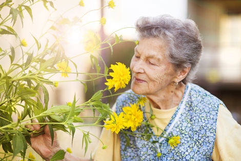 an elderly woman smells a flower