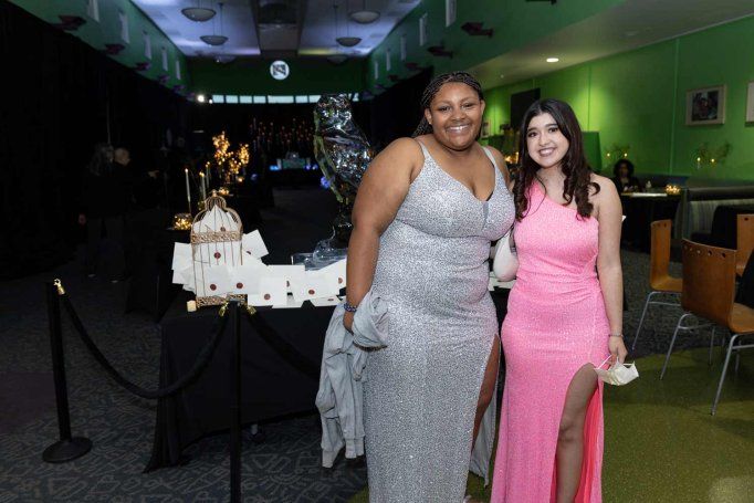 Two teenage girls pose together at the U C S F Benioff Children's Hospital prom event. One has a silver evening gown, and the other a pink one.