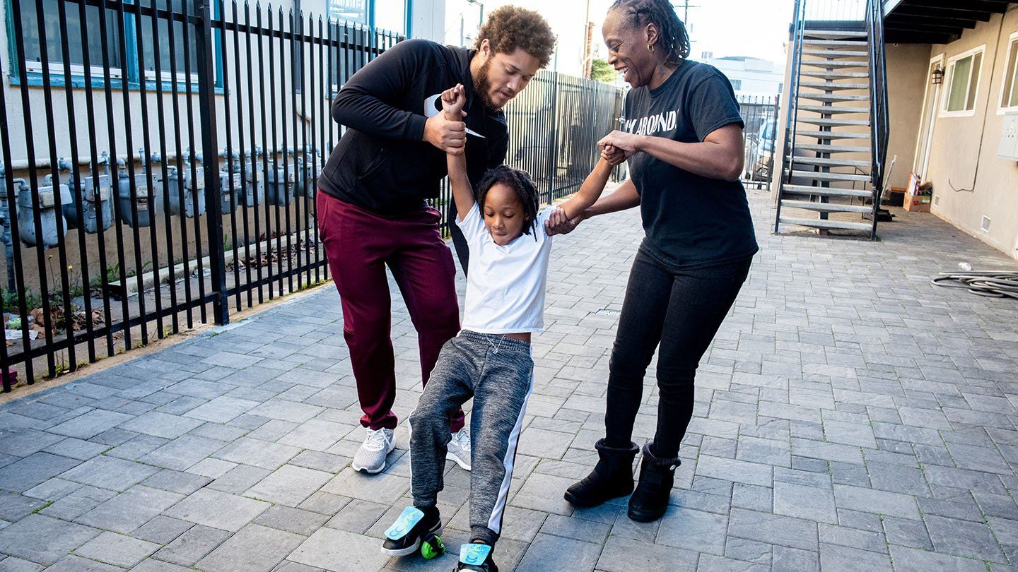 Rashetta Higgins and her older son hold opposite arms of her youngest son as he balances on rollerskates