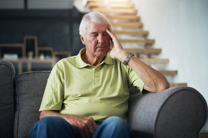 Elderly man sitting on couch with hand touching head