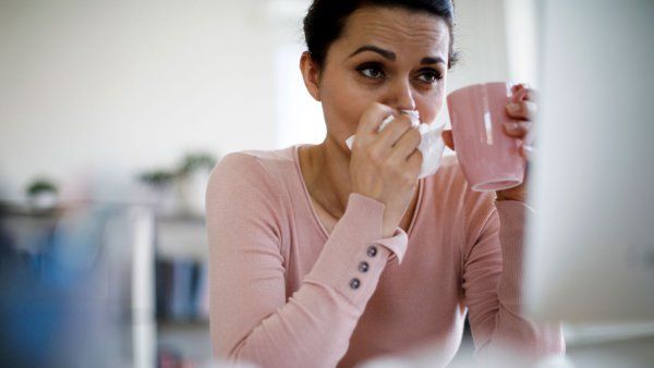 Woman blowing nose and holding mug