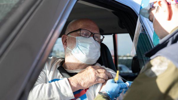 Older man in car about to receive a vaccine in his left arm