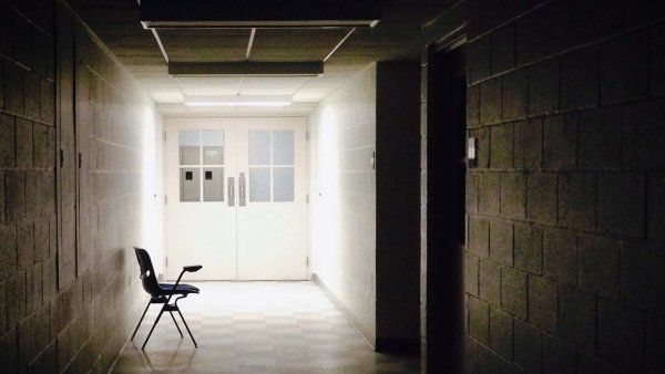 A dark school hallway with an empty chair at the far end.