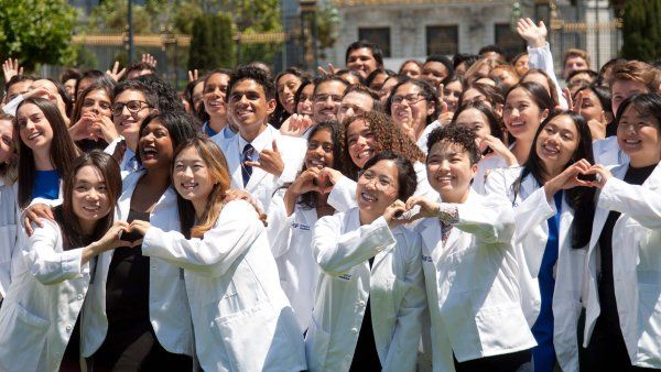 School of Medicine students donned in white coats pose for a group picture by joining their hands together to form hearts