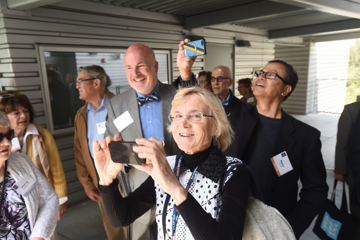 Susan Huscroft, MD (Medicine ’69), catches the camera's eye as she takes photographs with her smartphone during the Stem Cell Building Tours during Alumni Weekend. Flanking her are David Larwood, MS, PhD, JD, MBA (Graduate Division '83), left, and Mario Yco, MD (Medicine '79).
