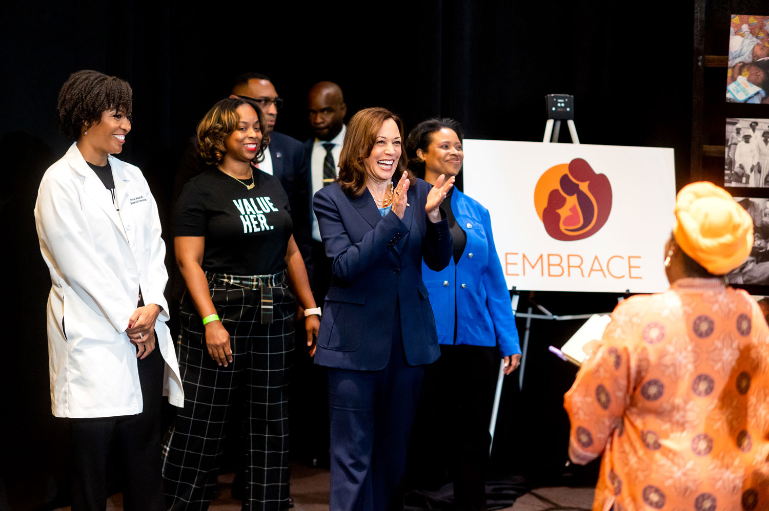 Vice President Kamala Harris with Black UCSF staff and faculty members. VP Harris is in the center, clapping. On the right-hand side is a sign with the orange EMBRACE logo