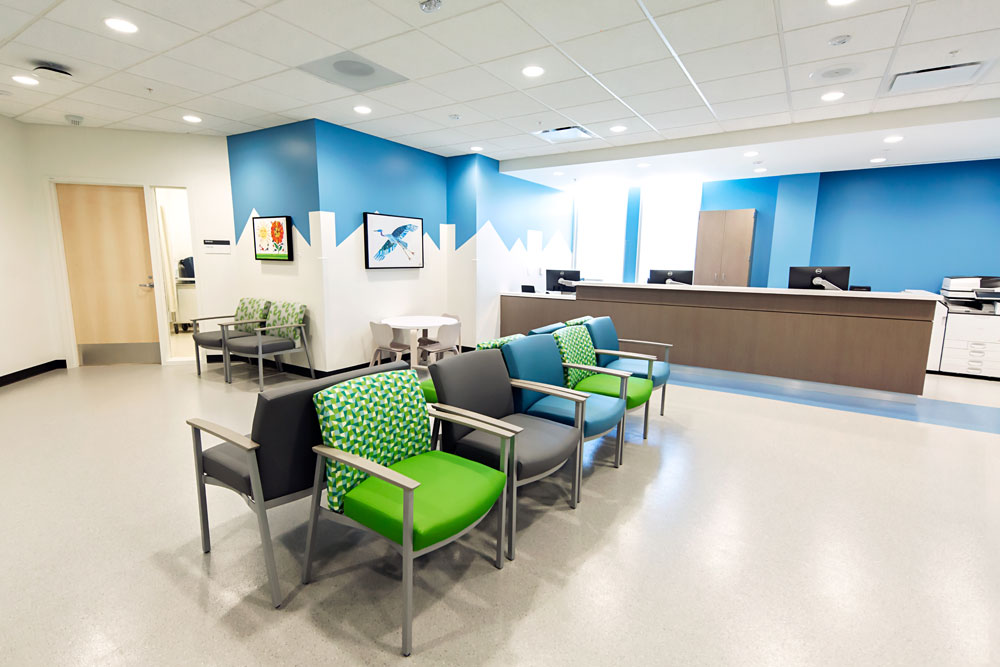 Lobby at Benioff Children's Hospital Walnut Creek Outpatient Center. Green and blue chairs are in the middle of the loby, with a blue and white wall behind a reception desk.