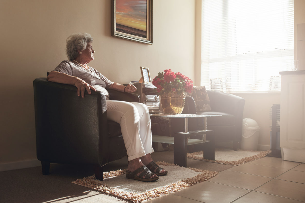 A senior woman sitting alone on a chair at home.