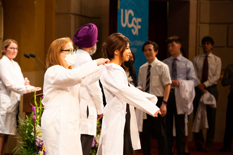 An incoming dentistry student receives her white coat from a faculty member onstage at the School of Dentistry white coat ceremony