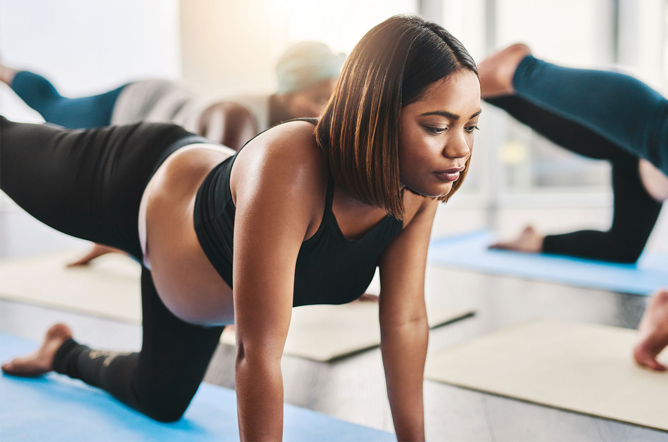 A young Black pregnant woman does exercises on a yoga mat along with other women