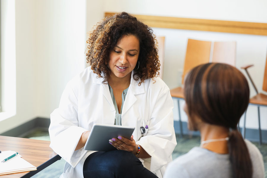 A Black female doctor holds a digital tablet as she consults with a female patient.