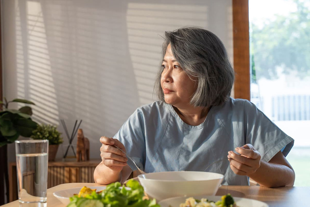 A middle-aged Asian woman eats alone at a dining table.