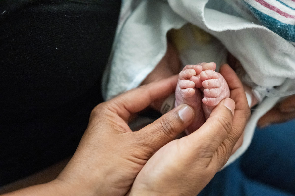 A pair of hands hold a newborn baby's feet.