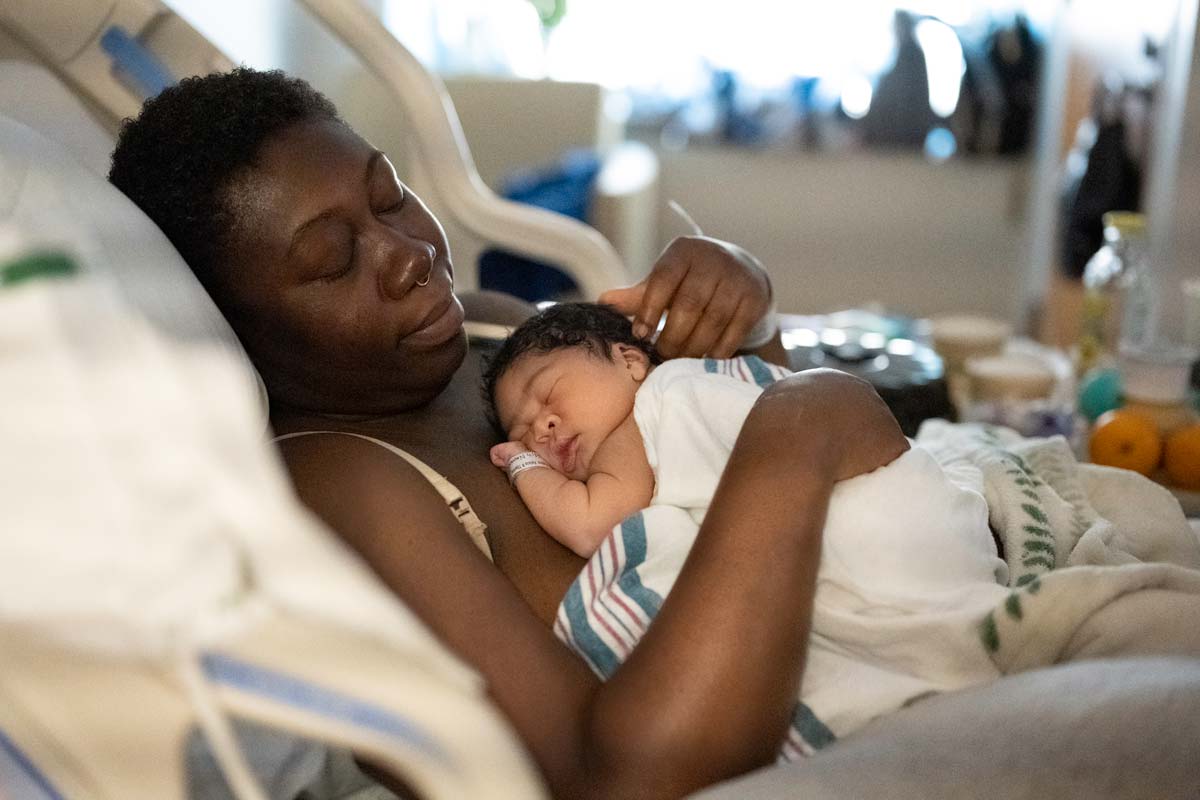 A Black mother tenderly holds her newborn son in a hospital bed.