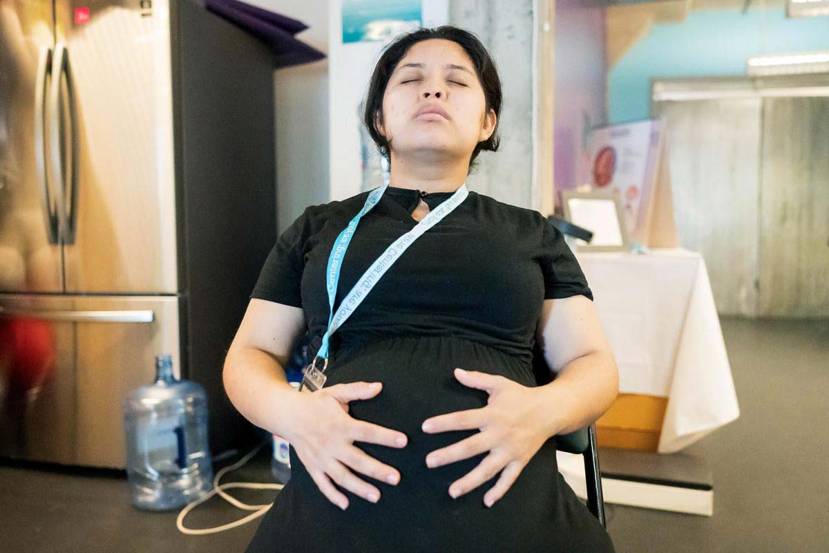 A pregnant woman of Hispanic descent holds her pregnant belly as she closes her eyes and meditates.
