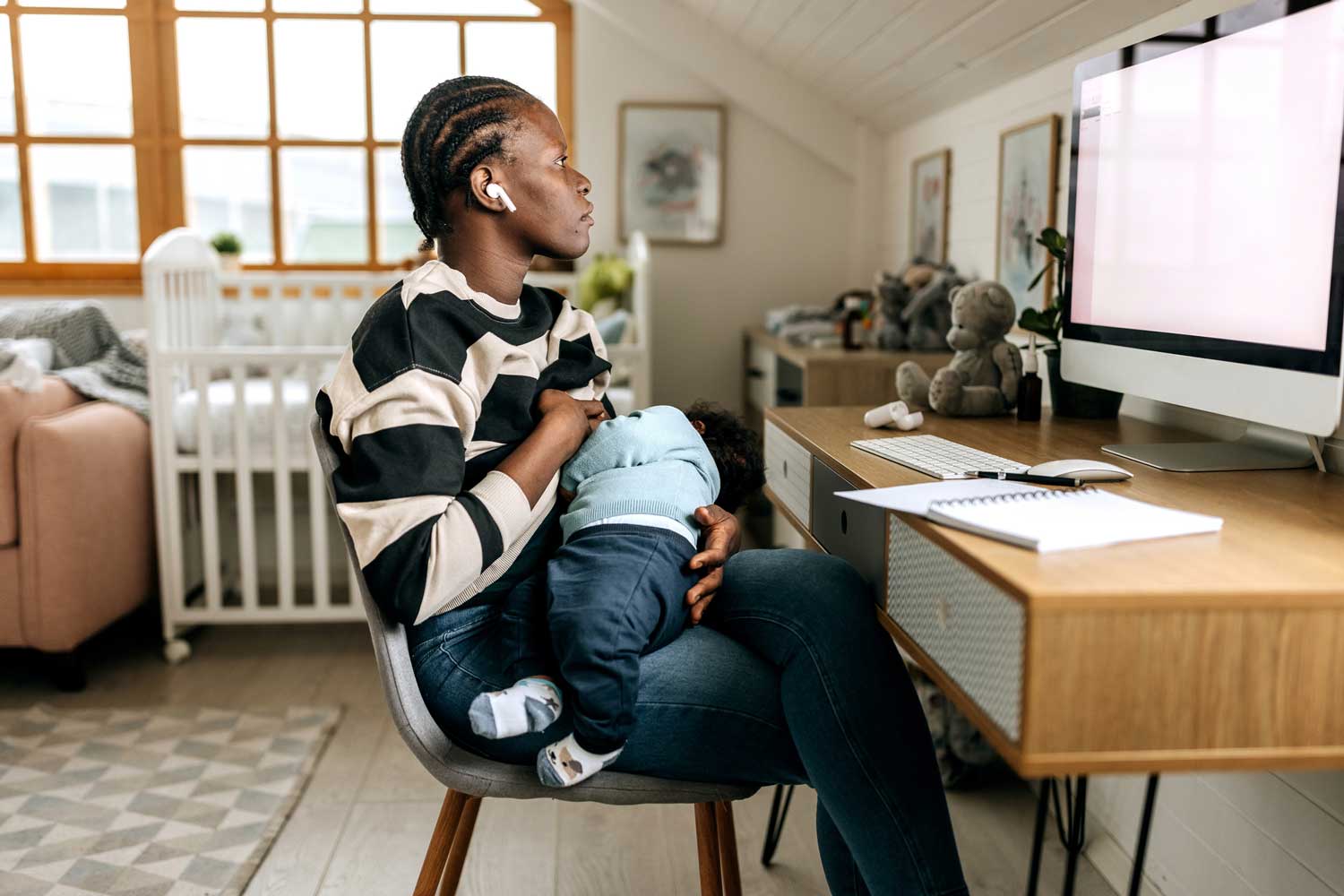 A mother working remotely breastfeeds her baby while looking at her work computer.