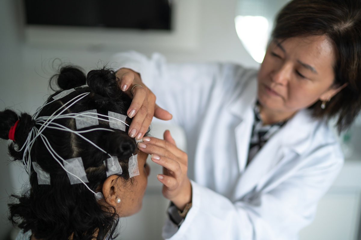 A female doctor places electrodes on a female patient's head for a sleep test polysomnography.