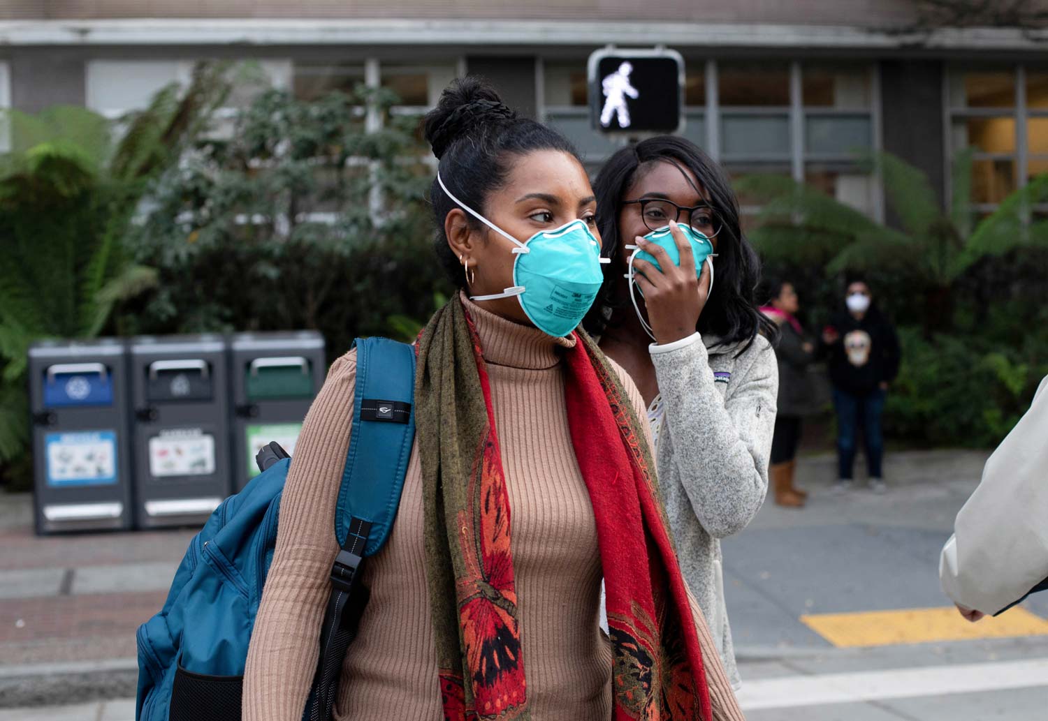 Two Black women stand outside wearing blue N95 face masks.