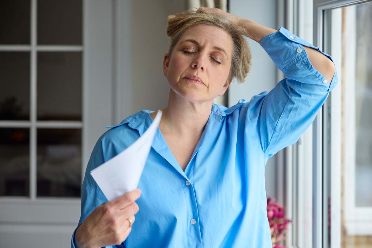 A Caucasian woman airs herself with a stack of papers and holds up her hair in order to cool down.