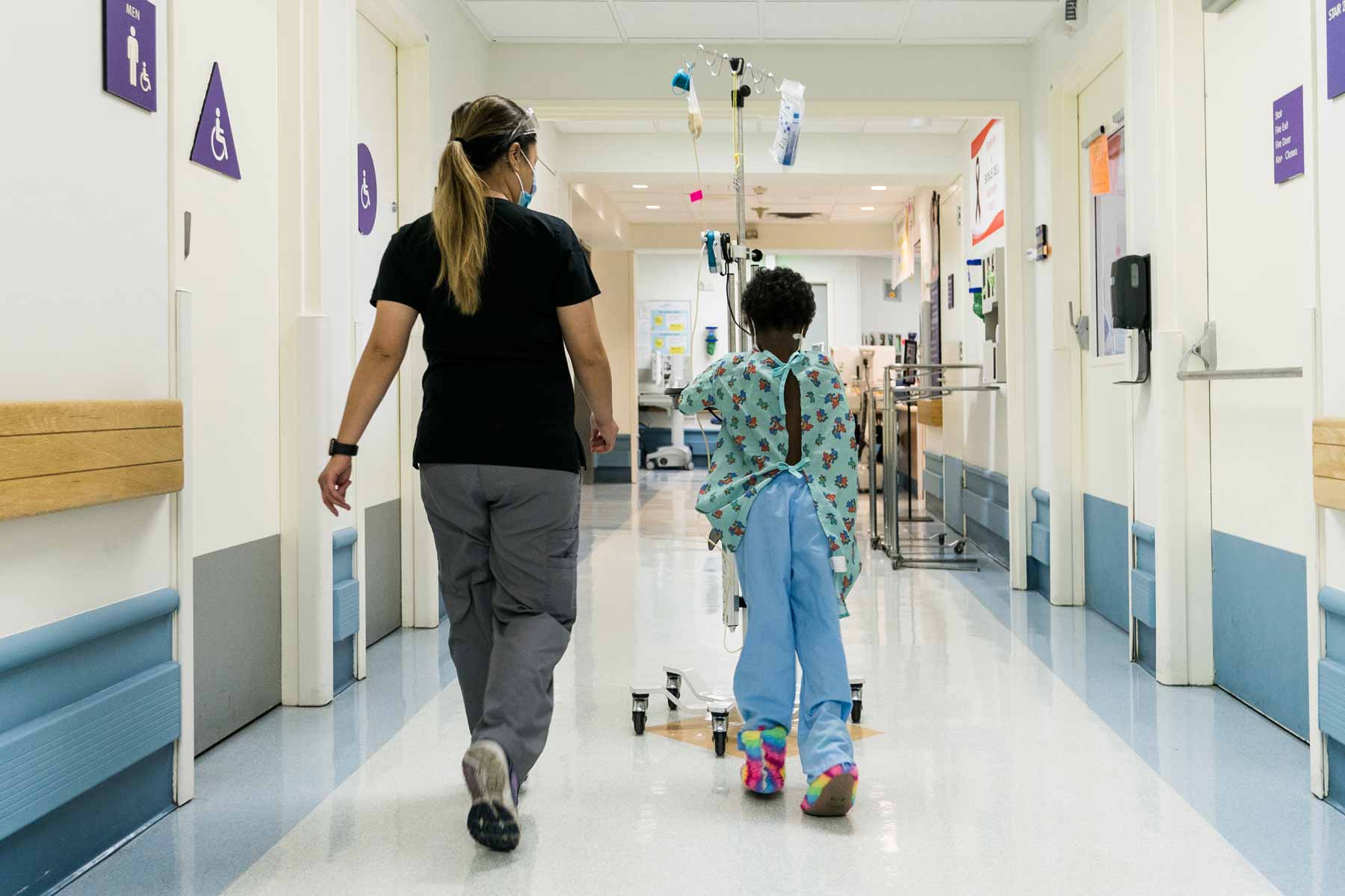 A UCSF staffmember walks with a young patient around the Pediatric Oncology unit at UCSF Childrens Oakland.