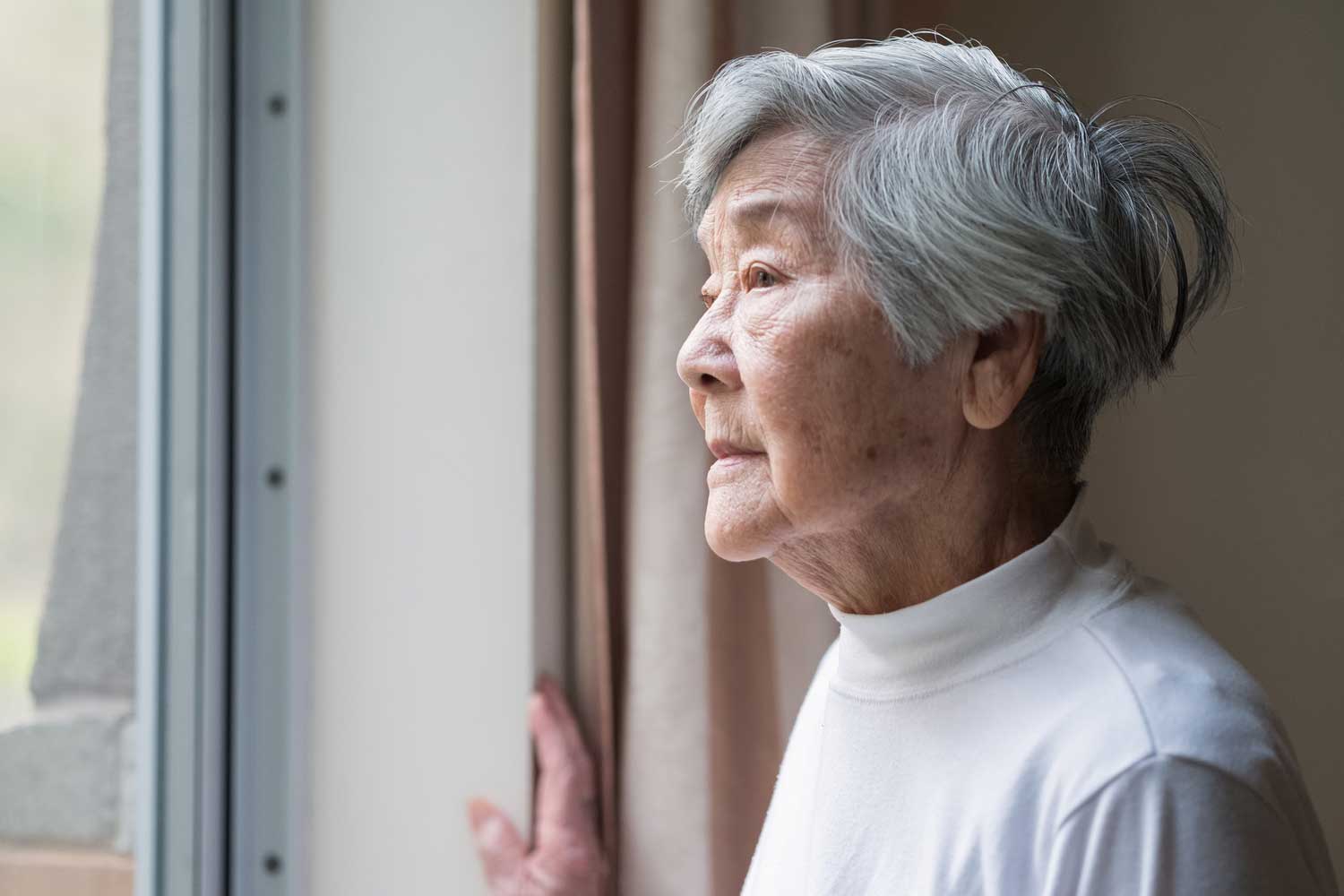 An elderly Asian woman stares wistfully out of a window.