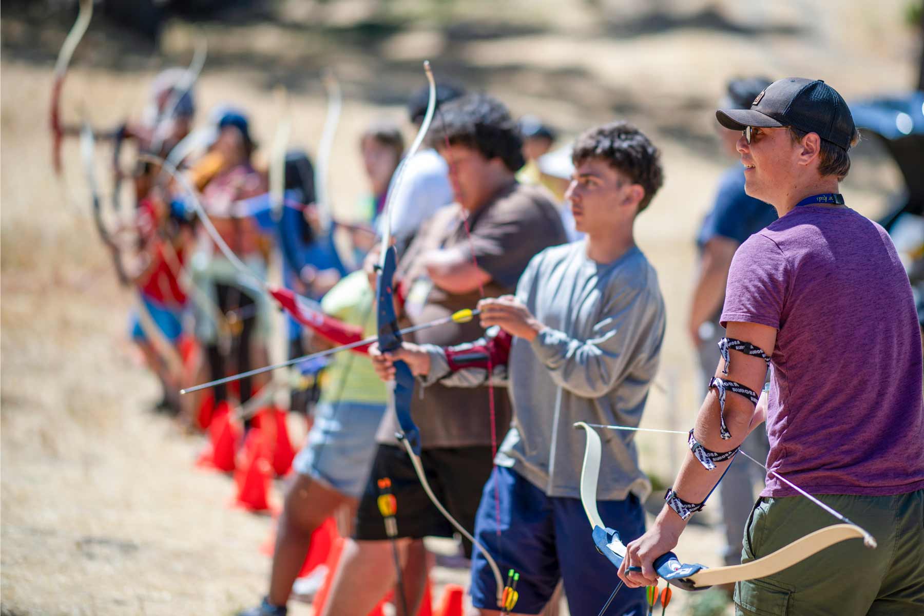 A group of teenagers with limb differences practices archery in a field.
