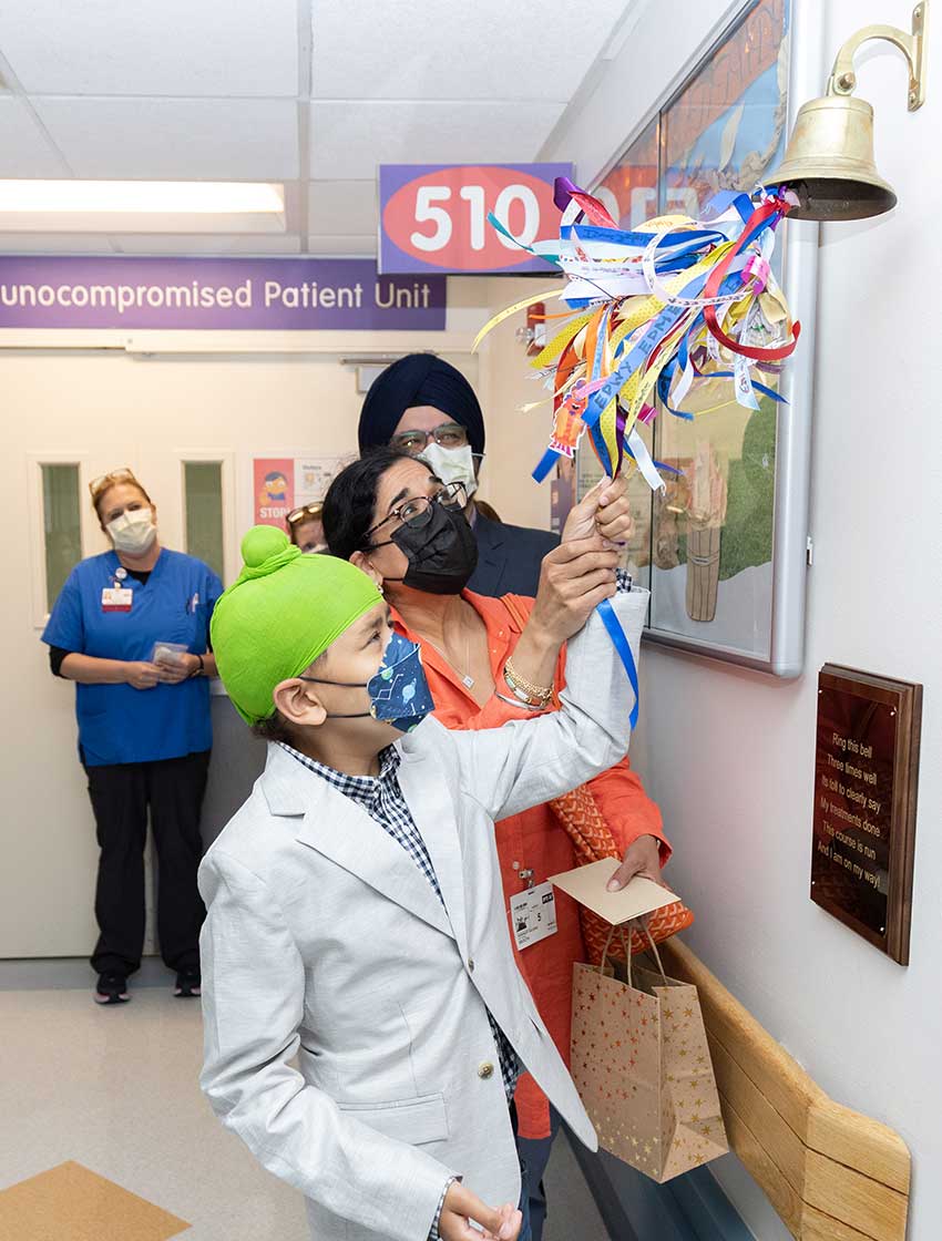 A young male patient named Manwar rings a bell at his remission celebration, along with his parents.
