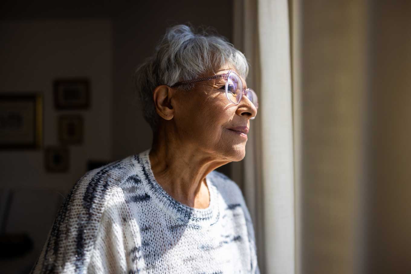A senior woman smiles as she gazes outside a window.