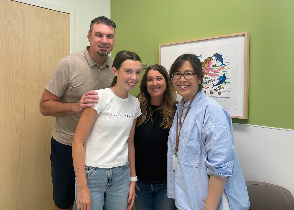 A young girl named Taylor smiles for a photo along with her parents and Dr. Vivien Nguyen in an examination room.