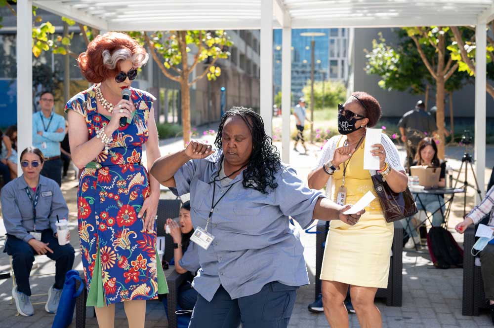 A female custodian employee dances as she receives a prize from a drag queen MC for a game of bingo.