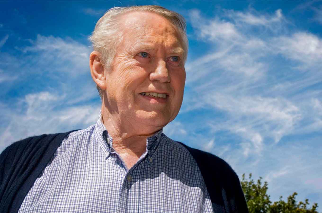 Chuck Feeney smiles as she stands under a blue sky.