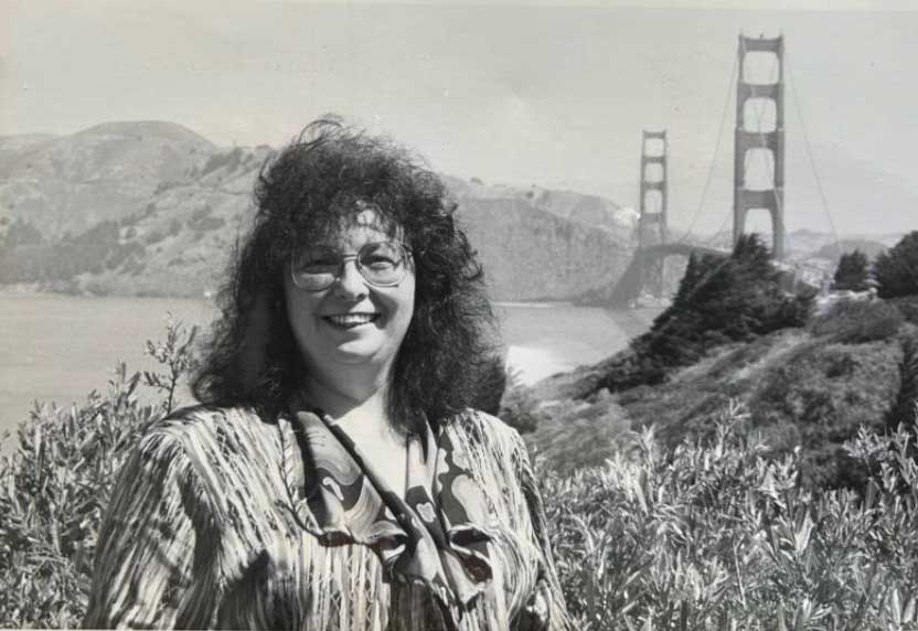 A black and white photo of Zena Werb standing in front of the Golden Gate Bridge.