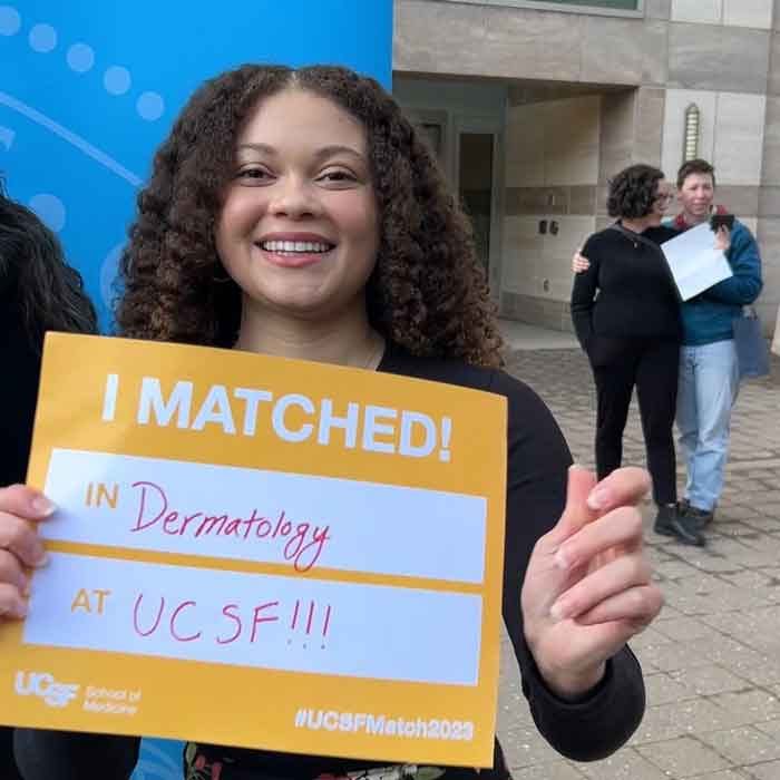A medical student holds up a sign that reads "Matched! Dermatology, UCSF" on Match Day.
