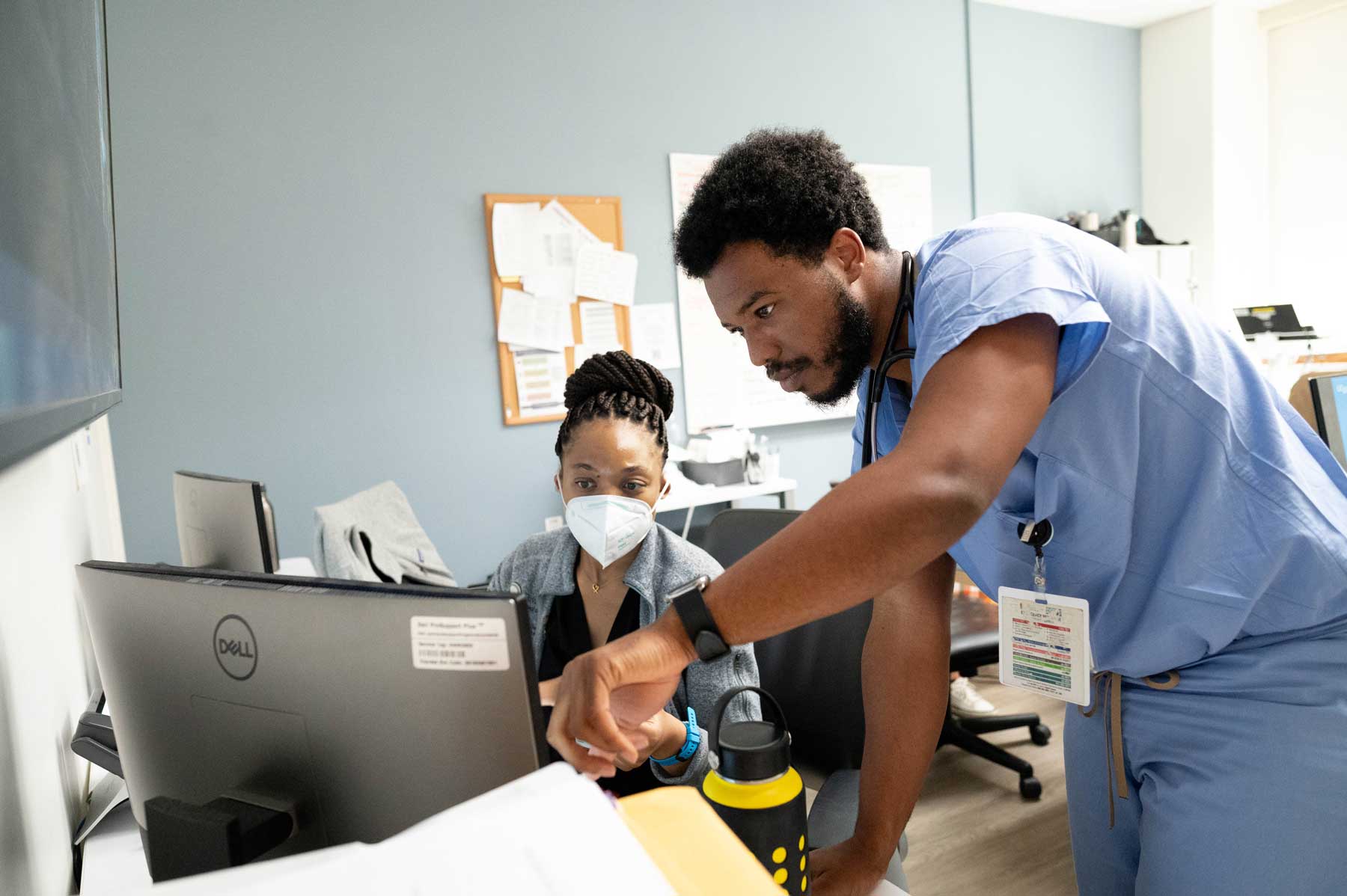 Two Black medical residents look at a computer. Kelechi (left) is a first-year resident, and Chris (right) is a senior resident.