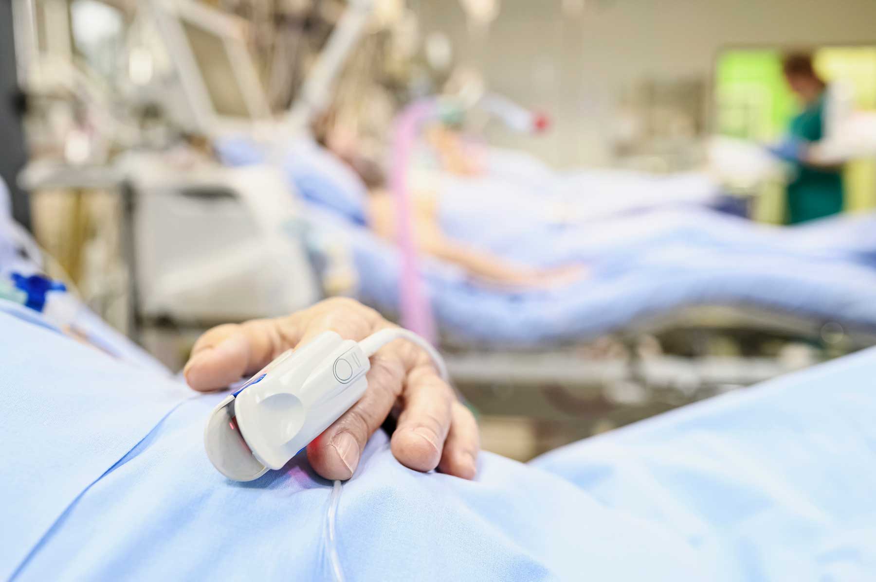 A patient wears a pulse oximeter as they lie in a hospital bed at an intenstive care unit.