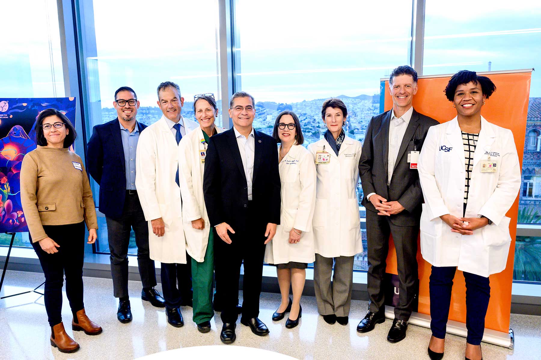 Xavier Becerra (center) stands with doctors and staff of UCSF and ANSIRH in front of large glass panes with the San Francisco cityscape in the background.