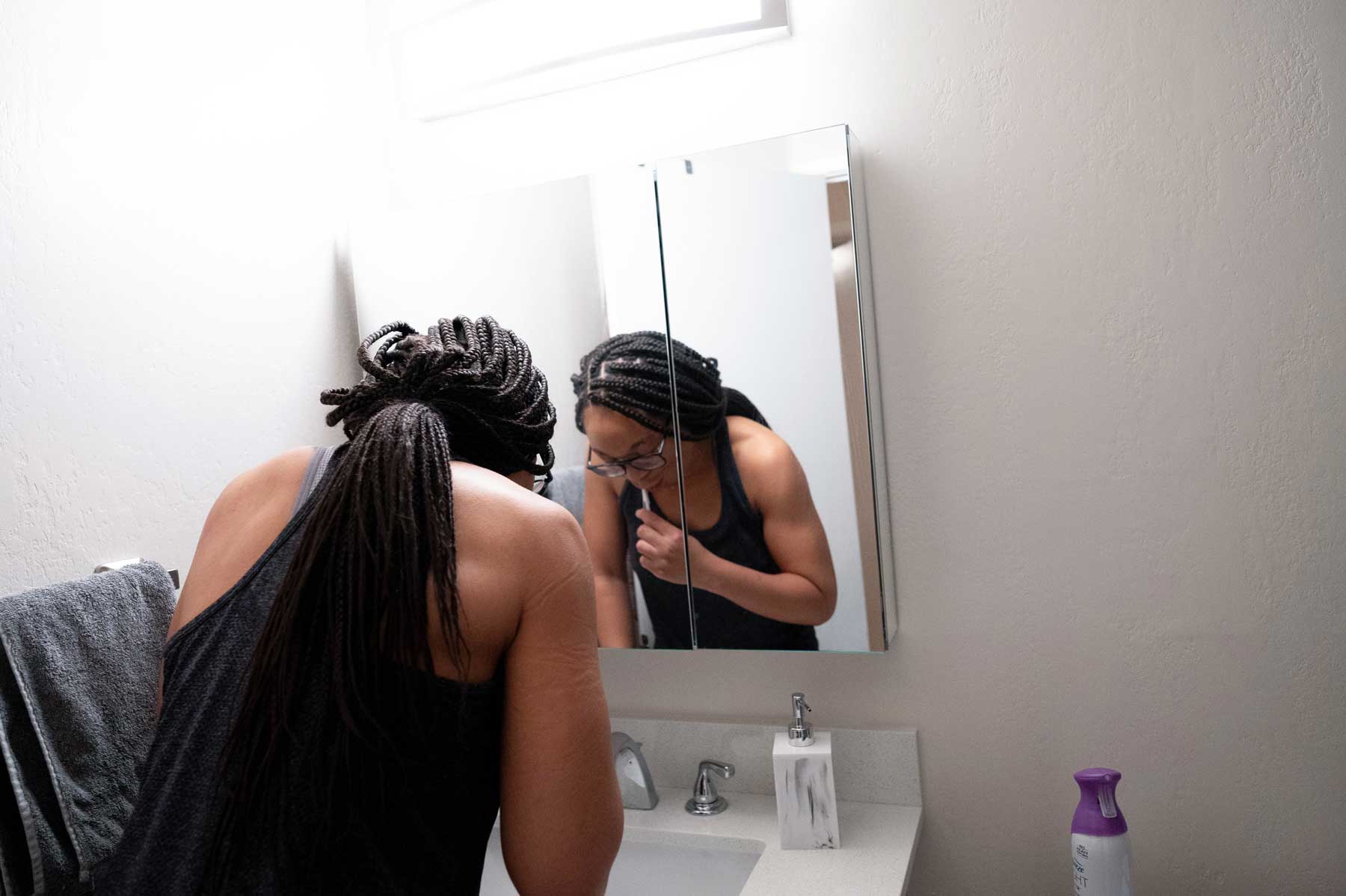 A young Black woman named Kelechi Okpara brushes her teeth over her bathroom sink early in the morning.
