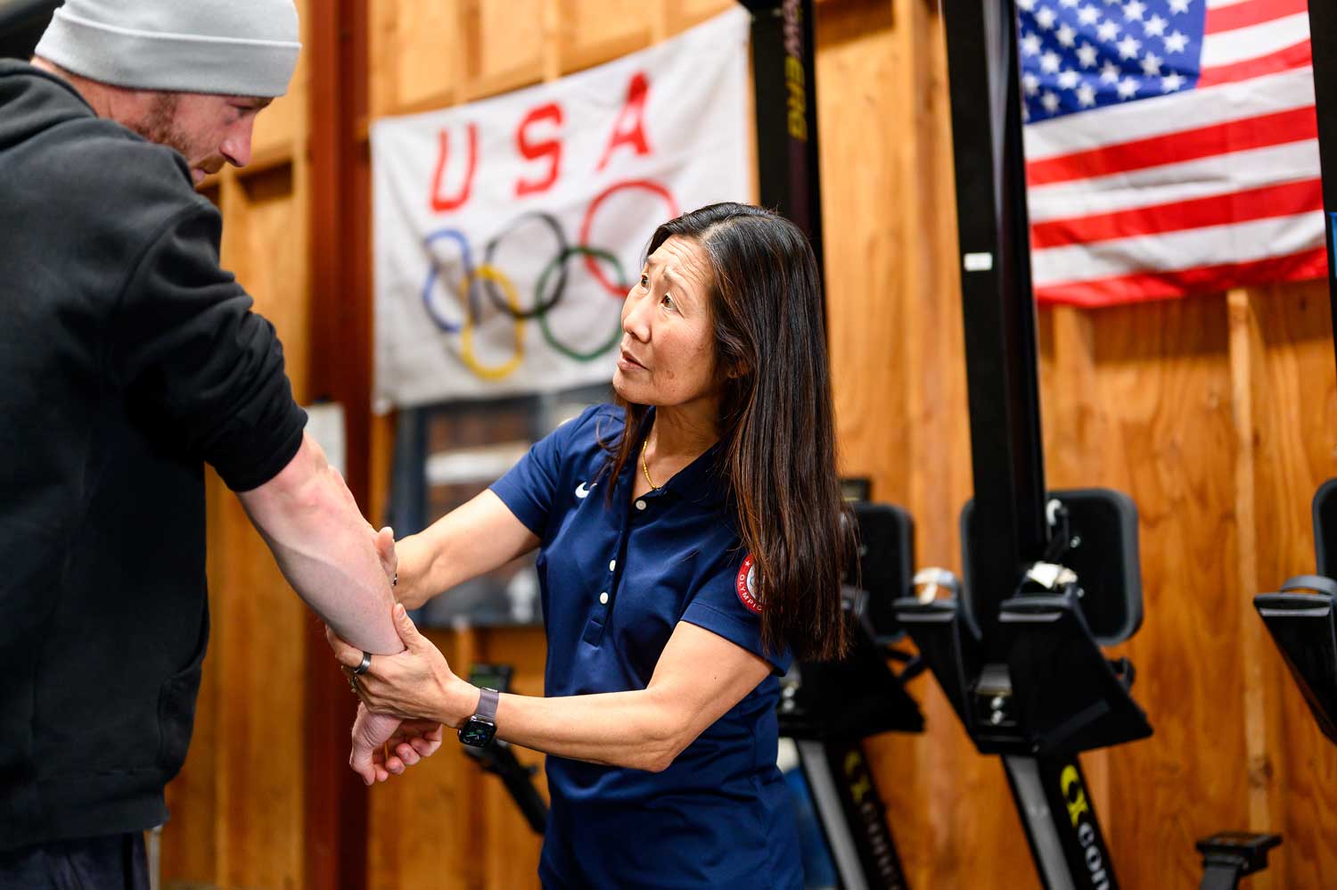 Ben Davison, left, receives physical therapy on his arm from Dr. Cindy Cang, right. On a wall in the background are an American flag and a Team USA Olympic flag.