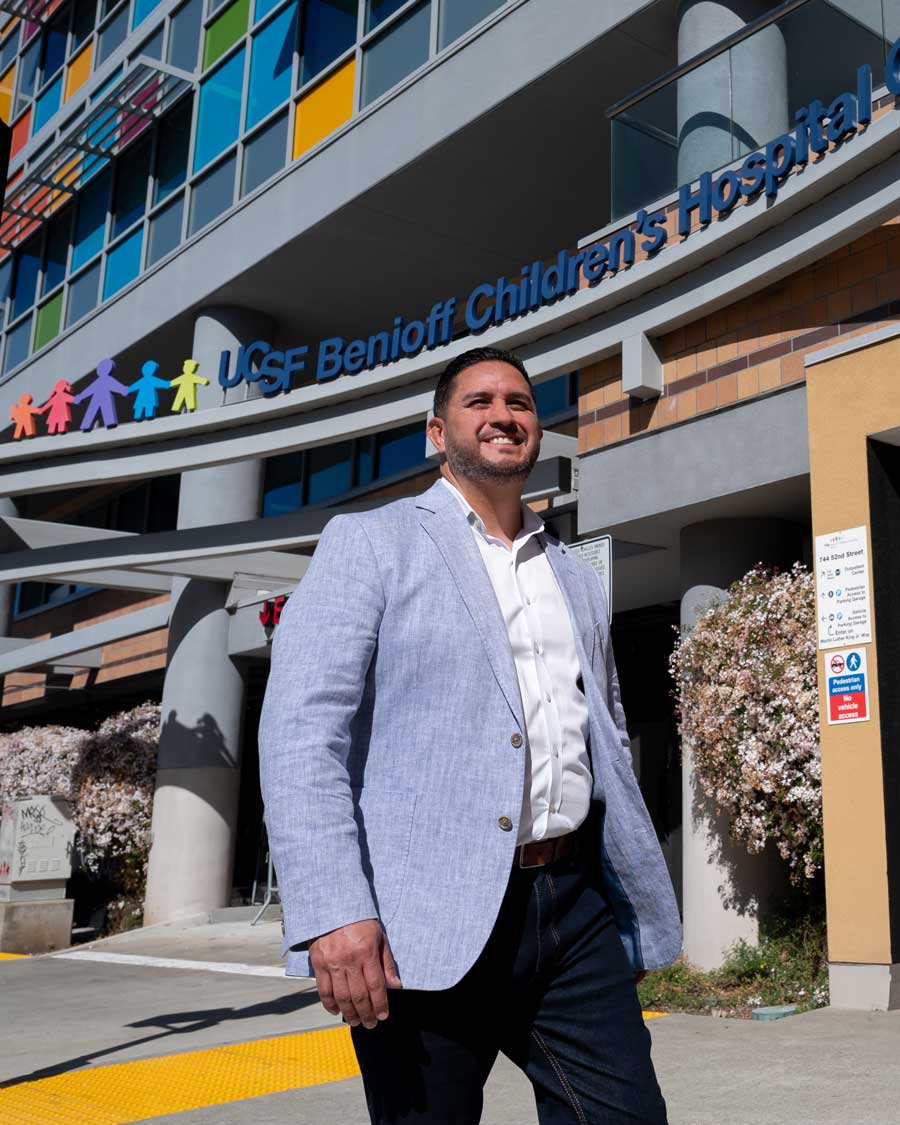 Michael Valero smiles as he walks in front of the colorful facade of the UCSF Benioff Children's Hospital Outpatient Center.
