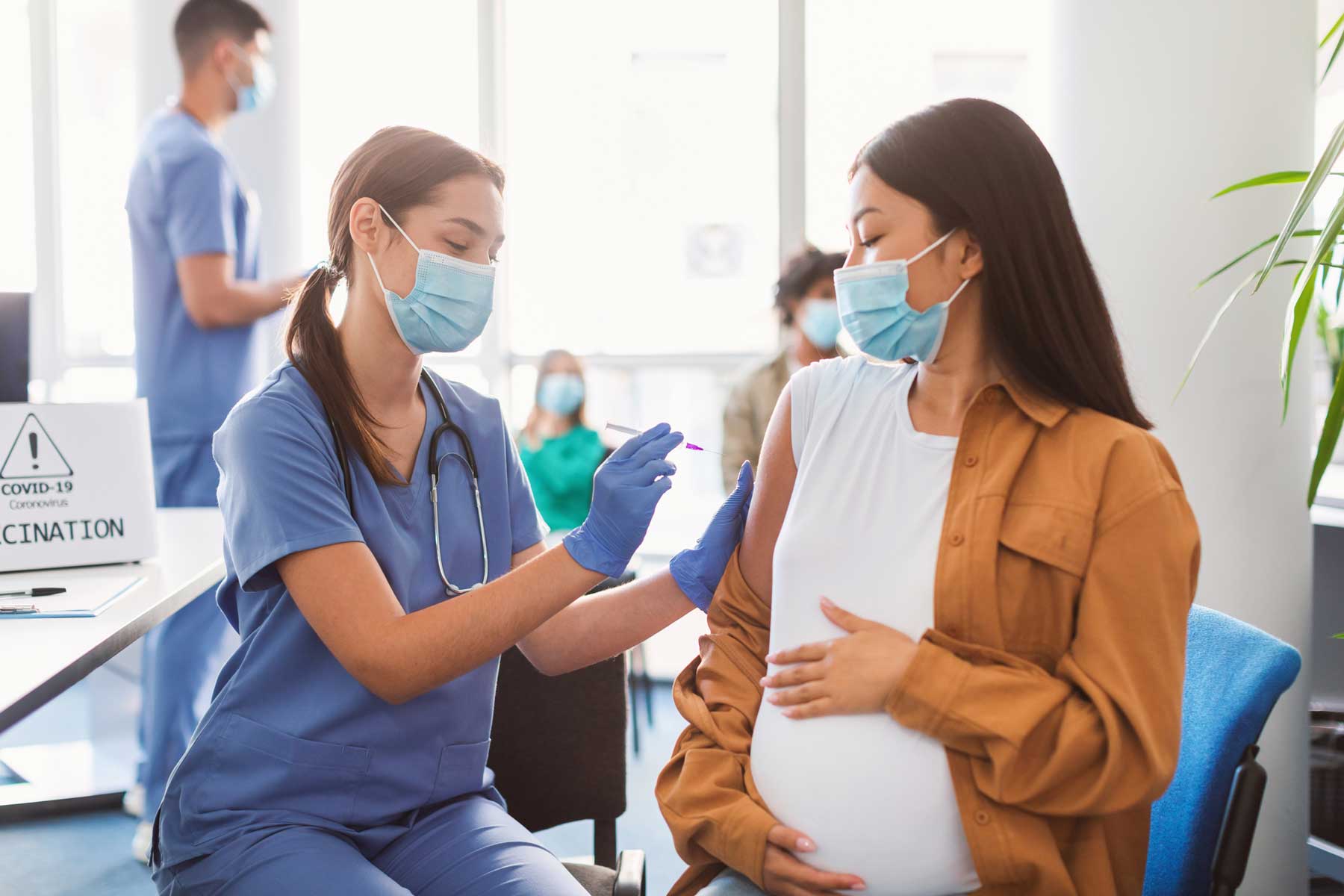 A pregnant woman wearing a surgical mask recieves a vaccine from a nurse.