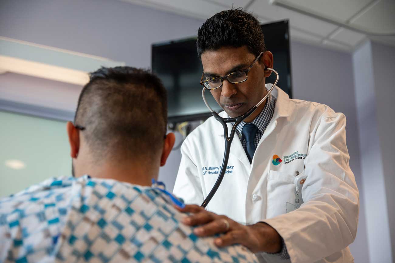 Dr. Anil Makam examines a male patient with a stethoscope at Zuckerberg San Francisco General Hospital.