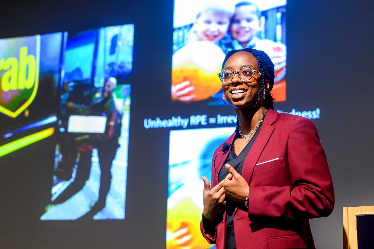 Sydney Williams presents her research onstage. Behind her is a projection screen with photos.