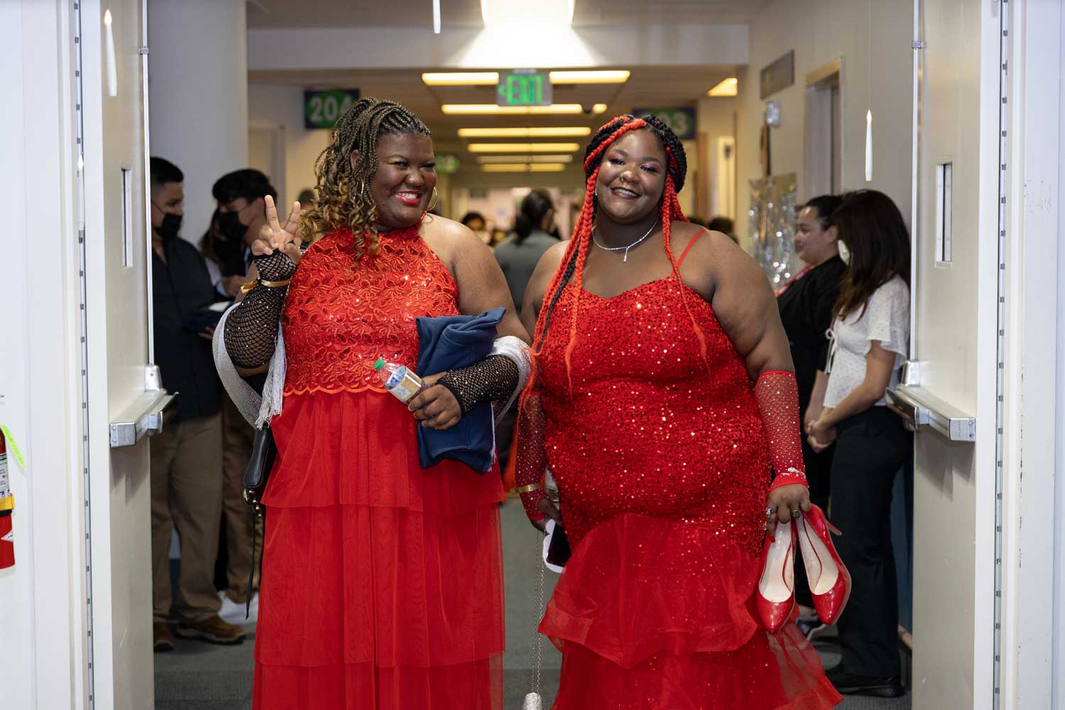 Two teenage girls wearing red prom dresses smile as they enter the prom event at U C S F Benioff Children's Hospital Oakland.