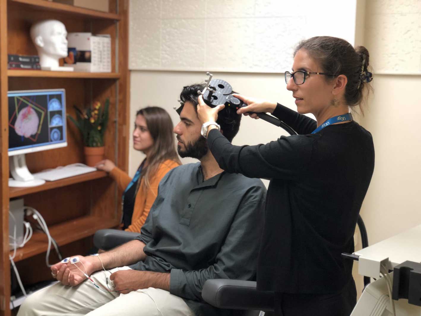 Psychiatrist Katherine Scangos adjusts a device over a man's head that is used for transcranial magnetic stimulation treatment.