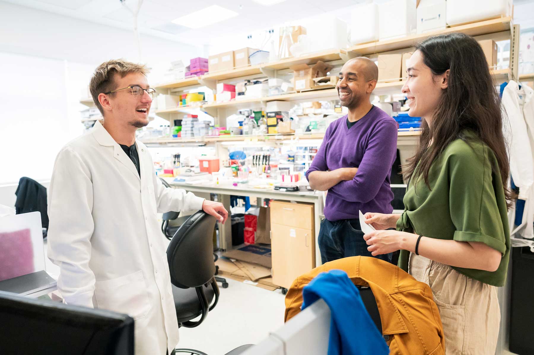 Corey Harwell smiles as he speaks with a visiting undergraduate student and a postdoctoral student in his lab.