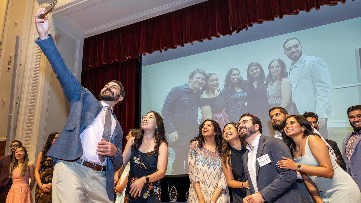 A group of graduates smile as they take a selfie on stage.